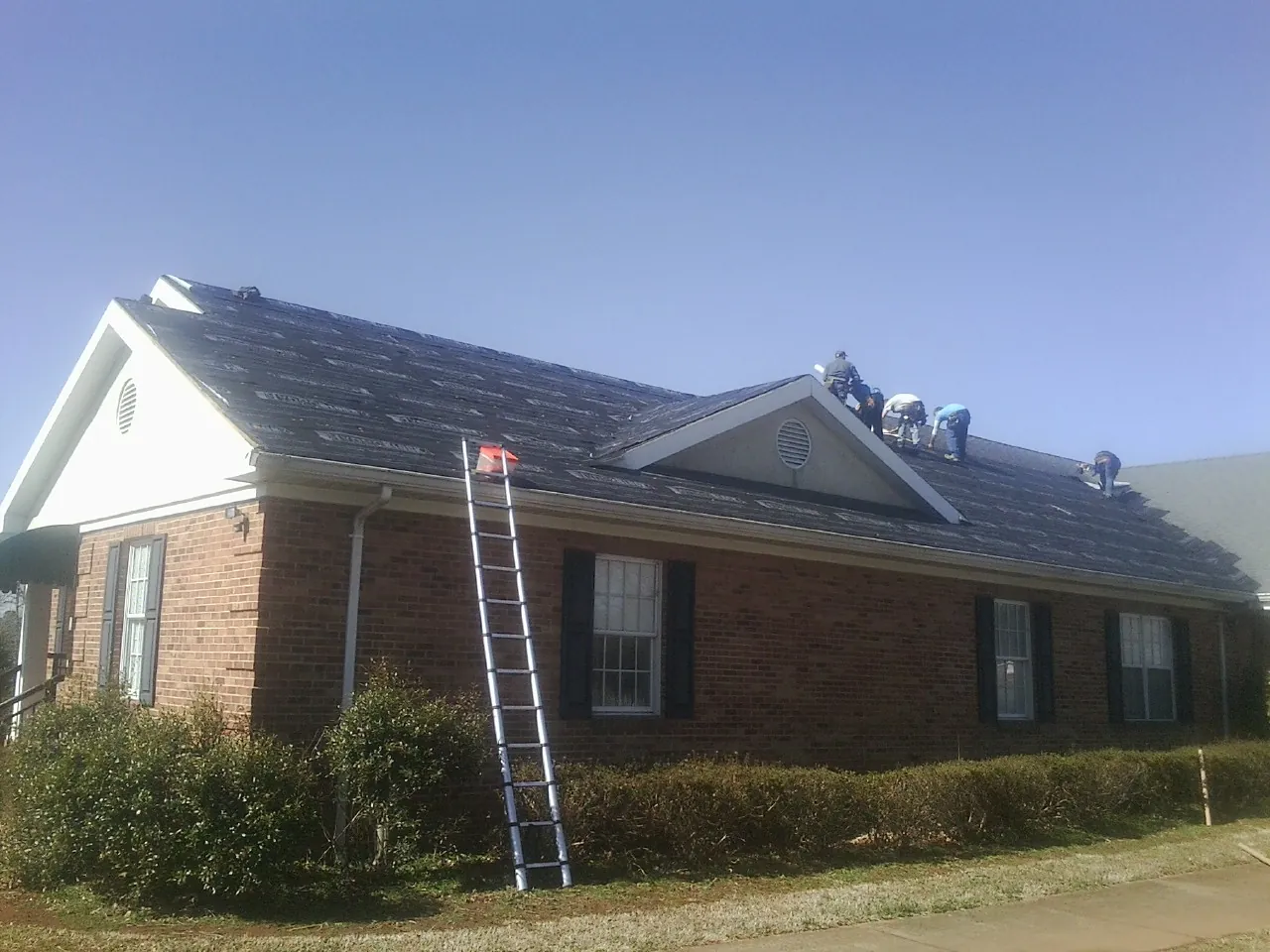 Crew tearing shingles off a brick ranch roof with a ladder set — Emergency Roof Repair work by our crew in Leechburg