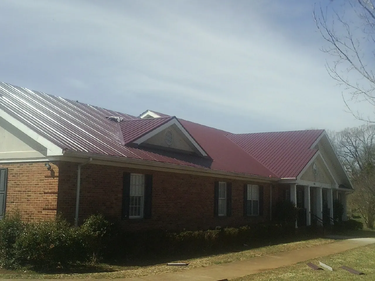 Red metal roof with gabled entries on a long brick building, from a Hail Damage Roof Repair job in Leechburg
