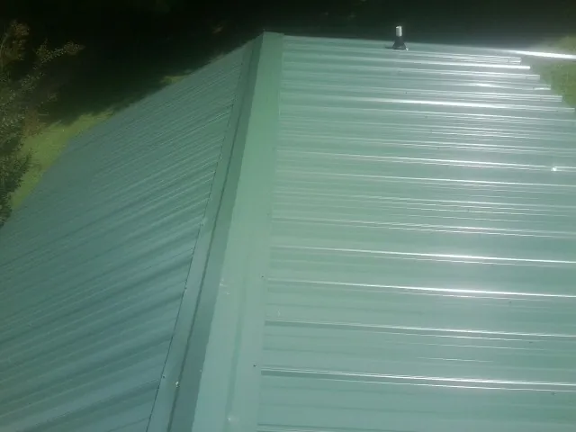 New green metal panels meeting at the ridge of a roof — Flat Roof Repair work by our crew in Leechburg