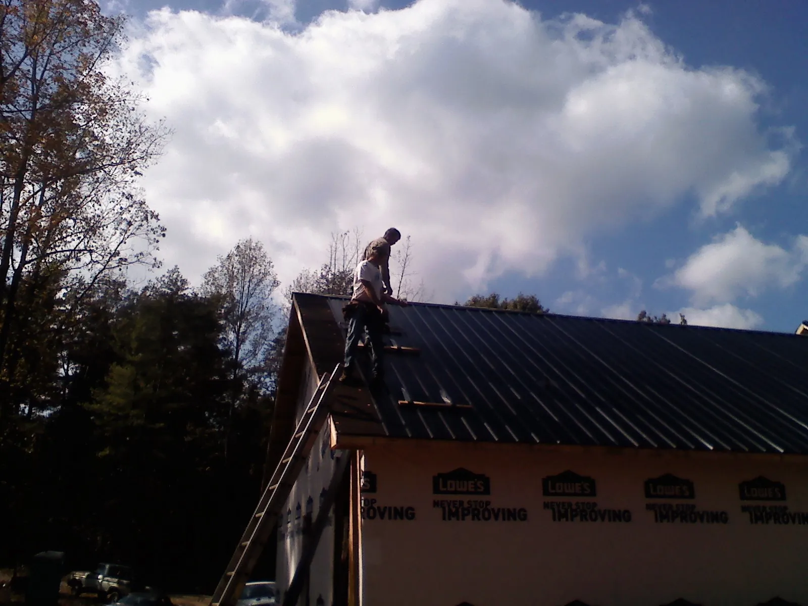 Roofer fastening dark metal panels high against a cloudy sky, from a Roof Inspection job in Leechburg