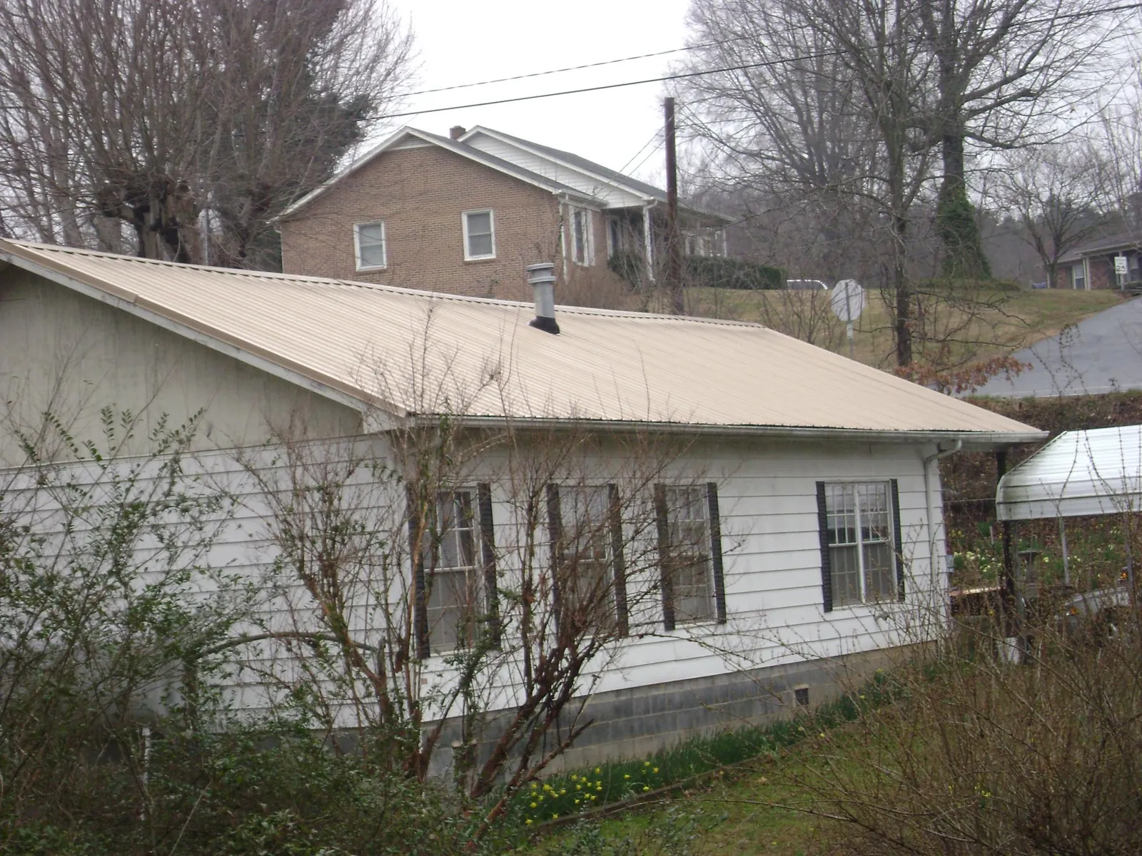 Tan metal roof on a white sided house set into a hillside — Commercial Roofing by Roofing Brothers in Leechburg